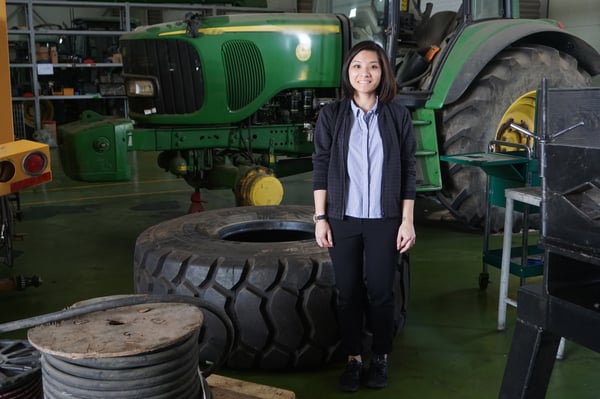 Image shows a woman standing in front of a big tractor and a huge tire