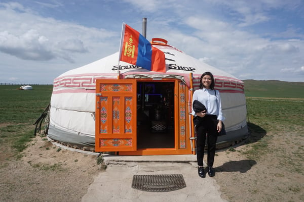 Image shows a woman standing in front of a ger with a Mongolian flag