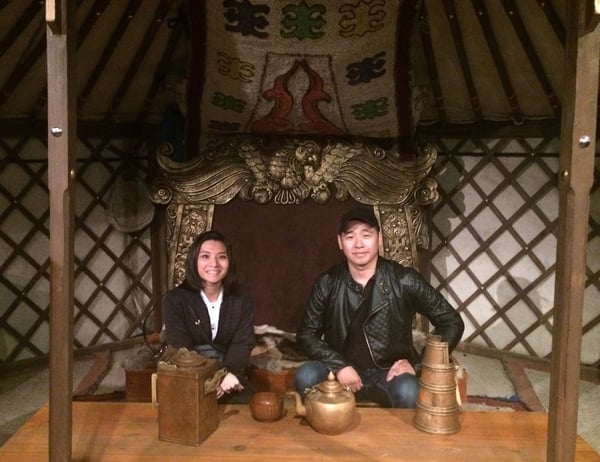 Image shows a woman and a man sitting inside a hut