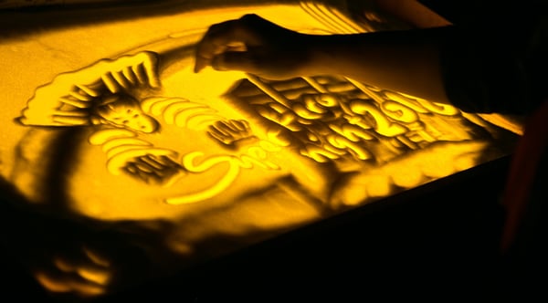 Image shows a hand over a sand artwork showing Superhero Night 2018