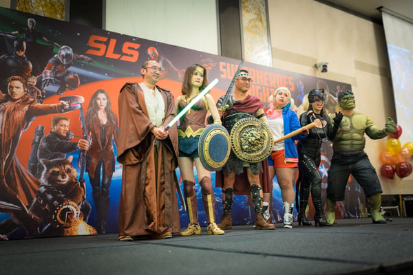 Image shows a group of people on stage dressed as superheros
