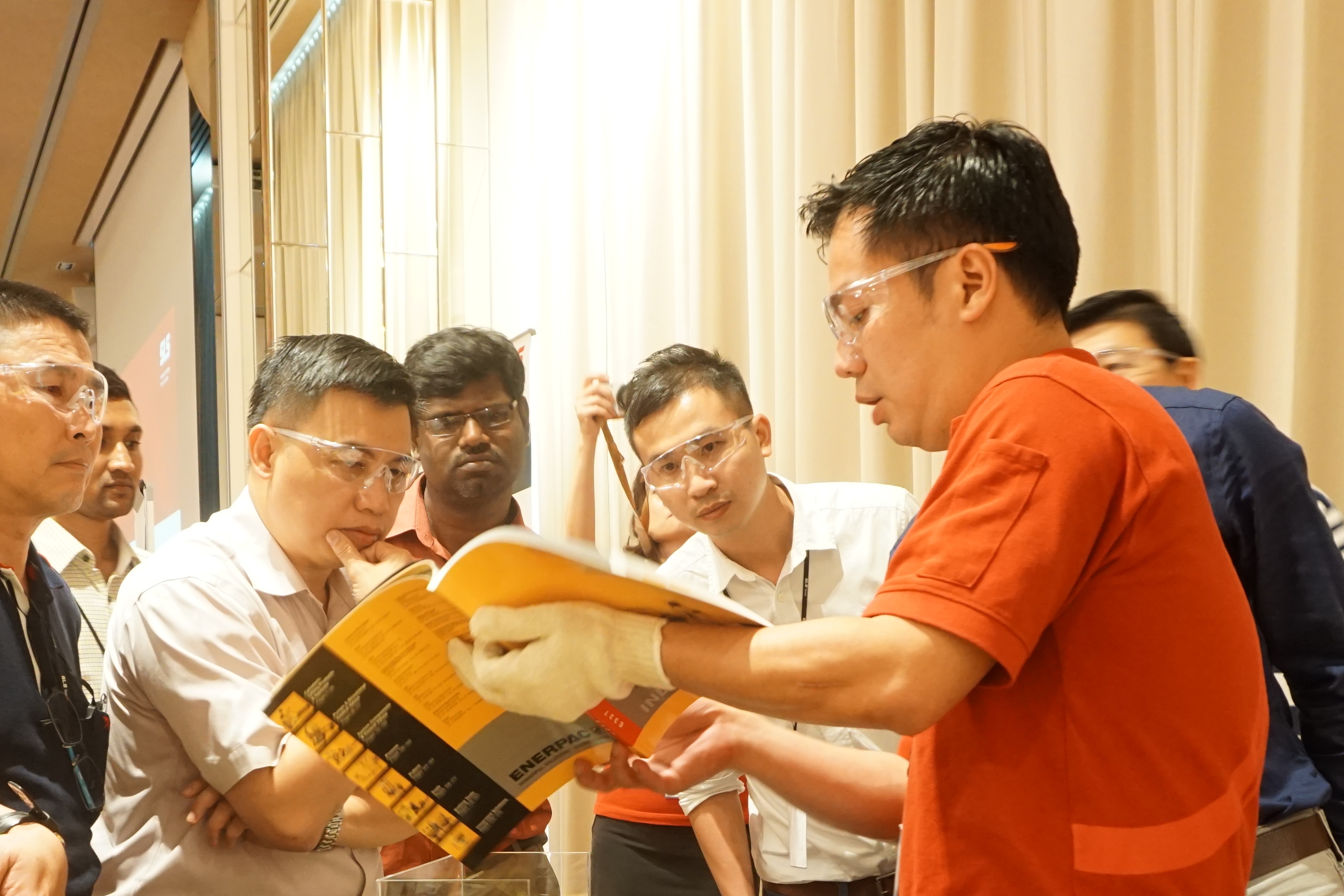 Image shows an SLS engineer showing an Enerpac product catalog to a group of customers